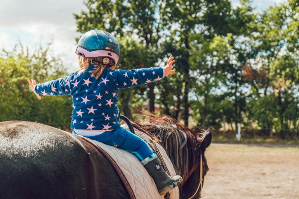 Little kid riding a black horse in an arena with trees in the background.